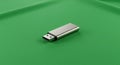 A metallic USB flash drive is placed on a smooth, solid green surface. The flash drive is Royalty Free Stock Photo