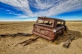 Metallic wrecked old car in the middle of a dry and desolated field under the blue sky Royalty Free Stock Photo