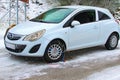Driver of white Opel Corsa is trying to mount snow chains on his car in wintry environment.