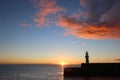 Mevagissey lighthouse at sunrise beneath red tinted clouds. Sun leaves a bright path over the sea. South coast, Cornwall UK