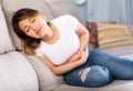 Mexican female at sofa holding hands on the illness stomache