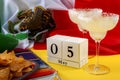 Mexican fiesta and Cinco de Mayo party concept theme with block calendar set on May 5th, traditional rug or serape, two margaritas