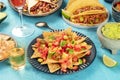 Mexican food with nachos in front and taco shells with pulled pork, burritos, guacamole and other dishes, with tequila and lime