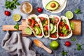 Mexican grilled chicken tacos with avocado, tomato, onion on rustic stone table. Recipe for Cinco de Mayo party.