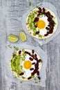 Mexican huevos rancheros tacos. Breakfast tostadas with black beans, avocado, fried egg, microgreens, sriracha ketchup. Top view