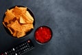 Mexican nachos in a black bowl with hot salsa dip sauce and tv remote on black background Royalty Free Stock Photo