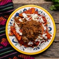 Mexican red chilaquiles with chilorio and cheese on wooden background