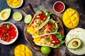 Mexican shrimp tacos with avocado, tomato, mango salsa on rustic stone table. Recipe for Cinco de Mayo party.