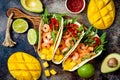 Mexican shrimp tacos with avocado, tomato, mango salsa on rustic stone table. Recipe for Cinco de Mayo party.