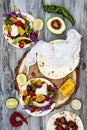 Mexican tacos with avocado, slow cooked meat, grilled corn, red cabbage slaw and chili salsa on rustic stone table.