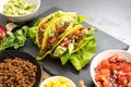 mexican tacos and some ingredients like fried ground beef, tomato salsa, guacamole, corn and herbs on a dark slate plate with cop