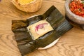 Mexican tamale of cochinita pibil stewed inside corn cob leaf with volcanic stone molcajete filled with pico de gallo Royalty Free Stock Photo