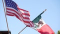 Mexican tricolor and American flag waving on wind. Two national icons of Mexico and United States against sky, San Diego, Royalty Free Stock Photo