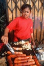 A Mexican woman barbequing hot dogs,