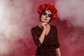 Mexican woman in la muerta attire and skull makeup during halloween with smoke.