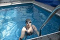 Woman floating in the pool moving legs and arms in the water to keep afloat practice swimming training with use of cloth cap and g