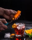 Mezcal Negroni cocktail preparation. Italian aperitivo. Orange peel is burnt in hands.