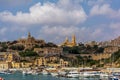 Yachts, boats and ships in Mgarr harbour, at Gozo, Malta, with Lourdes Chapel and Ghajnsielem Parish Church on the hill.