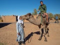 Mhamid, Morocco, North Africa : Transport camel with berber man and tourist in desert town, village tour