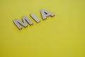 MIA wooden letters representing Missing In Action on yellow background