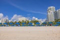 Miami\'s sandy beach with blue sunbeds and umbrellas, set against white buildings, all under blue sky with fluffy clouds. Royalty Free Stock Photo