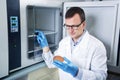 Microbiologist hand cultivating a petri dish whit inoculation loops, beside autoclave. Royalty Free Stock Photo