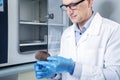 Microbiologist hand cultivating a petri dish whit inoculation loops, beside autoclave.