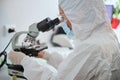 Microbiologist in a hazmat suit observing a microscopic specimen