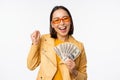 Microcredit and money concept. Stylish asian young woman in sunglasses, laughing happy, holding dollars cash, standing Royalty Free Stock Photo