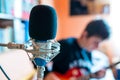 Microphone on focus, playing young guitarist on background in a small music studio Royalty Free Stock Photo