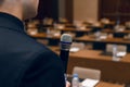 Microphone in hand of man in suit on background of empty conference hall. Rehearsal of public speaking Royalty Free Stock Photo