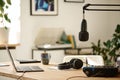 Microphone hanging over desk with headphones, soundboard and laptop