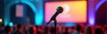Microphone positioned on stand ready for event presentation in front of large screen. Audience seated in background. Colorful Royalty Free Stock Photo