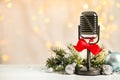 Microphone with red bow and decorations on white table against blurred lights, space for text