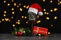 Microphone with Santa hat and decorations on grey stone table against blurred lights