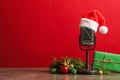 Microphone with Santa hat and decorations on grey table against red background. Christmas music