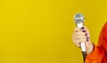Microphone in woman& x27;s hand on yellow background with space for text. Unrecognizable woman holding mic for singing.