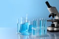 Microscope near different laboratory glassware and test tubes with light blue liquid on table Royalty Free Stock Photo