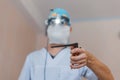 Microsurgeon man in a medical mask in a white robe in binocular loupes stands in the operating room and holds a surgical clip