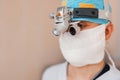 Microsurgeon man in a white mask in special medical clothes and glasses with binocular loupes in the operating room.