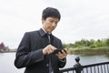 Mid adult Asian businessman using cell phone along river Royalty Free Stock Photo