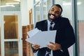 Mid adult bearded black man Entrepreneur Businessman wearing suit holding papers and talking on smartphone laughing