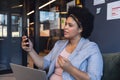 Mid adult biracial businesswoman talking on video call while sitting with laptop in office