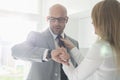 Mid adult businessman checking wristwatch while woman adjusting his tie at home