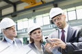 Mid adult businessman explaining machine part of colleagues in metal industry