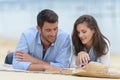 Mid-adult couple layed on beach looking at book