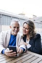 Mid adult couple looking at smartphone while sitting at outdoors table. Carefree senior man and woman using mobile phone Royalty Free Stock Photo