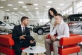 Mid-adult couple talking with sales agent and signing contract for new car in modern car showroom. Royalty Free Stock Photo