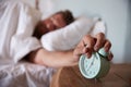 Mid adult man asleep in bed, reaching out to alarm clock on the bedside table in the foreground Royalty Free Stock Photo