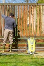 Mid adult man cleaning a wooden gate with a power washer. High water pressure cleaner used to DIY repair garden gate. Royalty Free Stock Photo